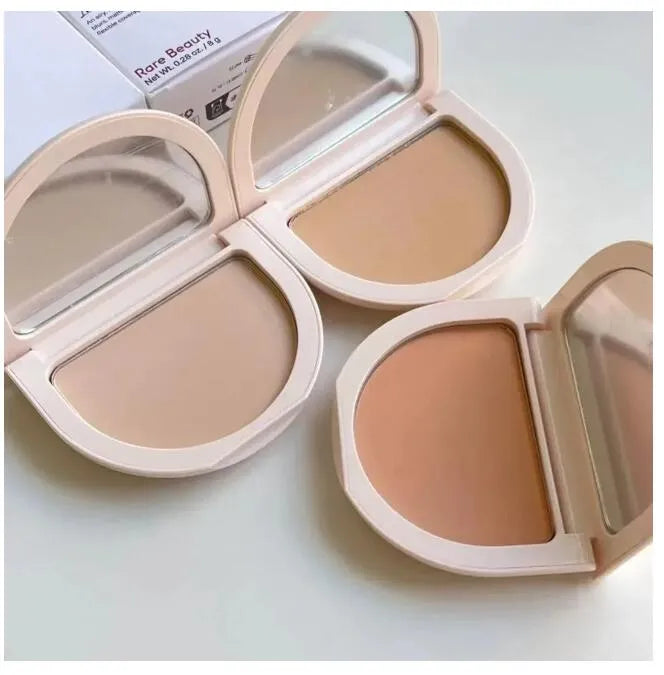 Two identical pressed powder compacts with mirrors open on a flat surface