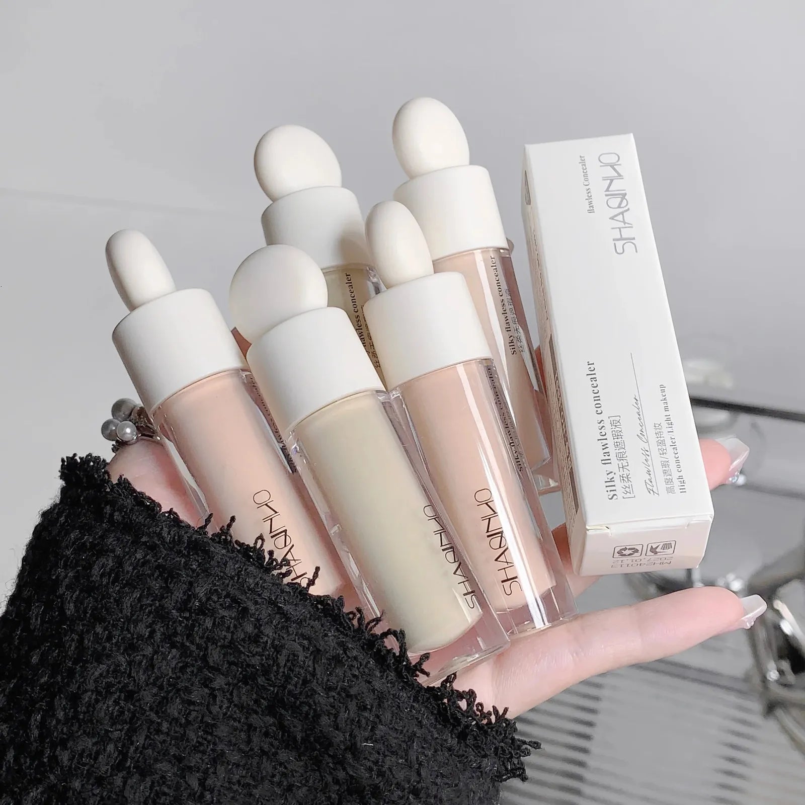 Liquid concealer bottle with applicator on a neutral background