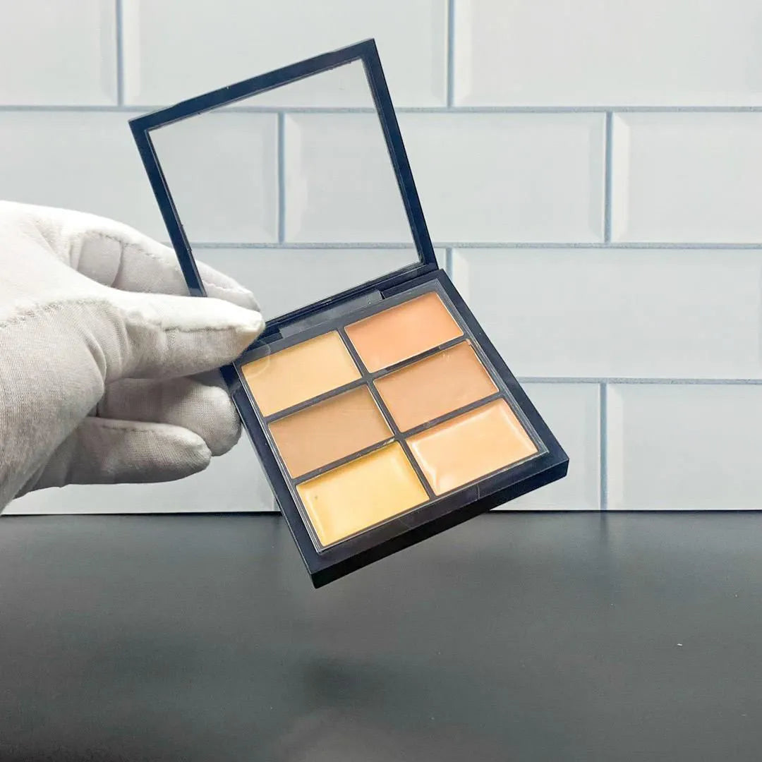 Open makeup palette showing six different concealer shades arranged in rectangular pans