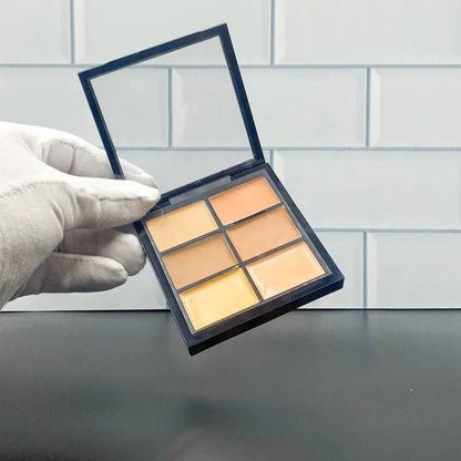 Open makeup palette showing six different concealer shades arranged in rectangular pans